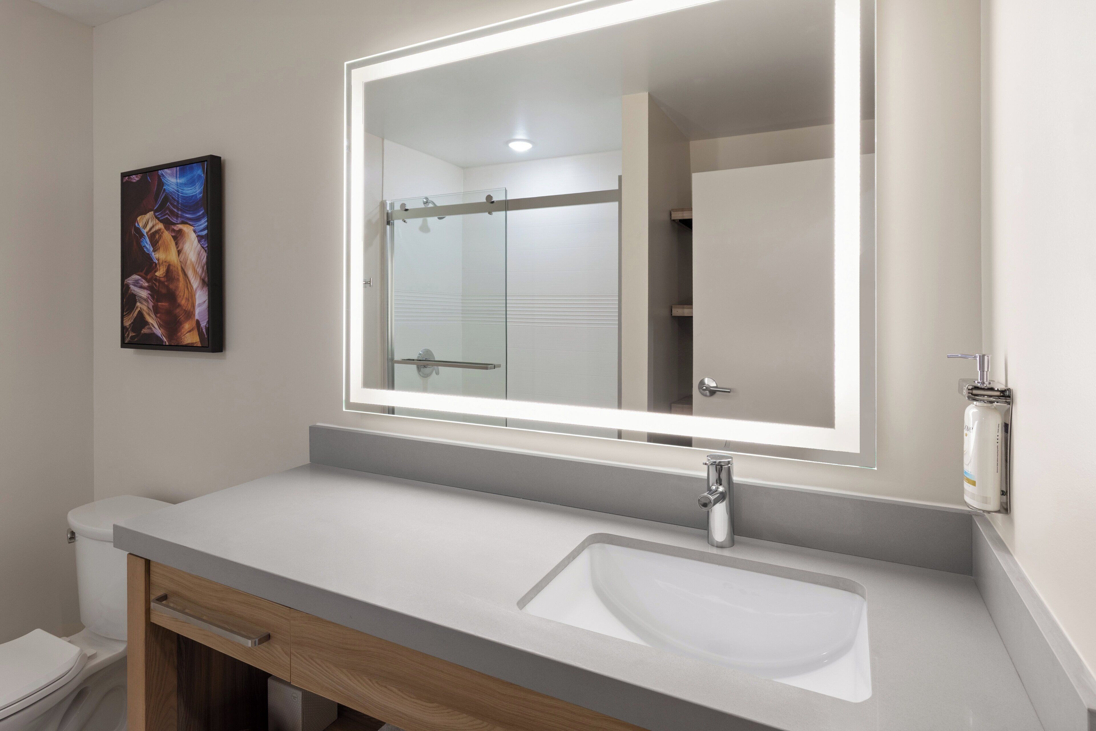A modern bathroom with a large mirror, a white sink, and a wooden cabinet.