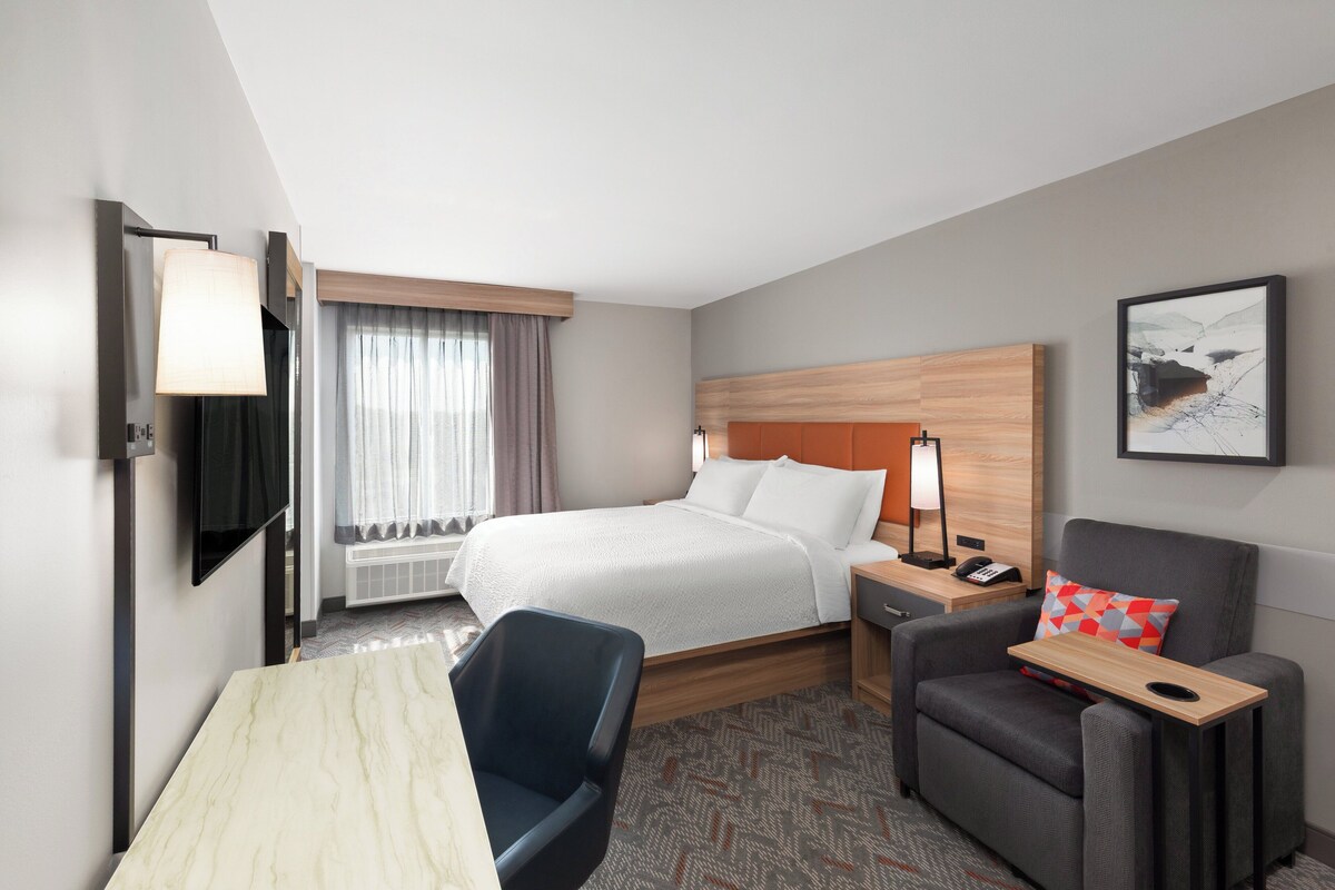 A hotel room with a bed, a desk, a chair, a nightstand, and a TV.