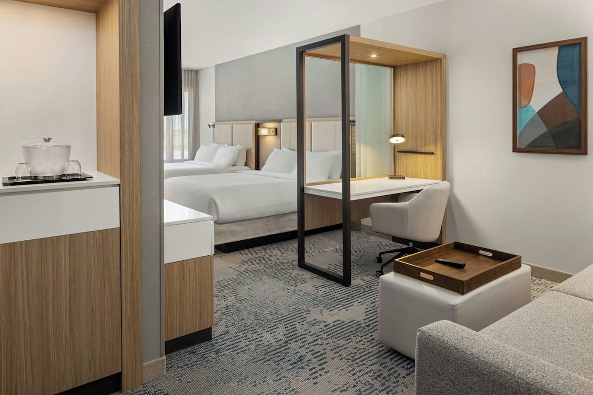 A hotel room with a bed, a desk, a chair, a small table with a tray, and a TV mounted on the wall.