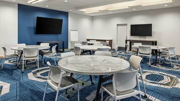 A conference room with multiple tables and chairs, a large flat-screen TV, and a whiteboard.