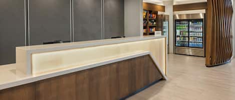 A reception area with a modern design, featuring a wooden reception desk, a patterned wall, and a refrigerated beverage display.