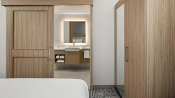 Habitación de hotel con un armario de madera, una cama, un baño con lavamanos y espejo, y una alfombra estampada.