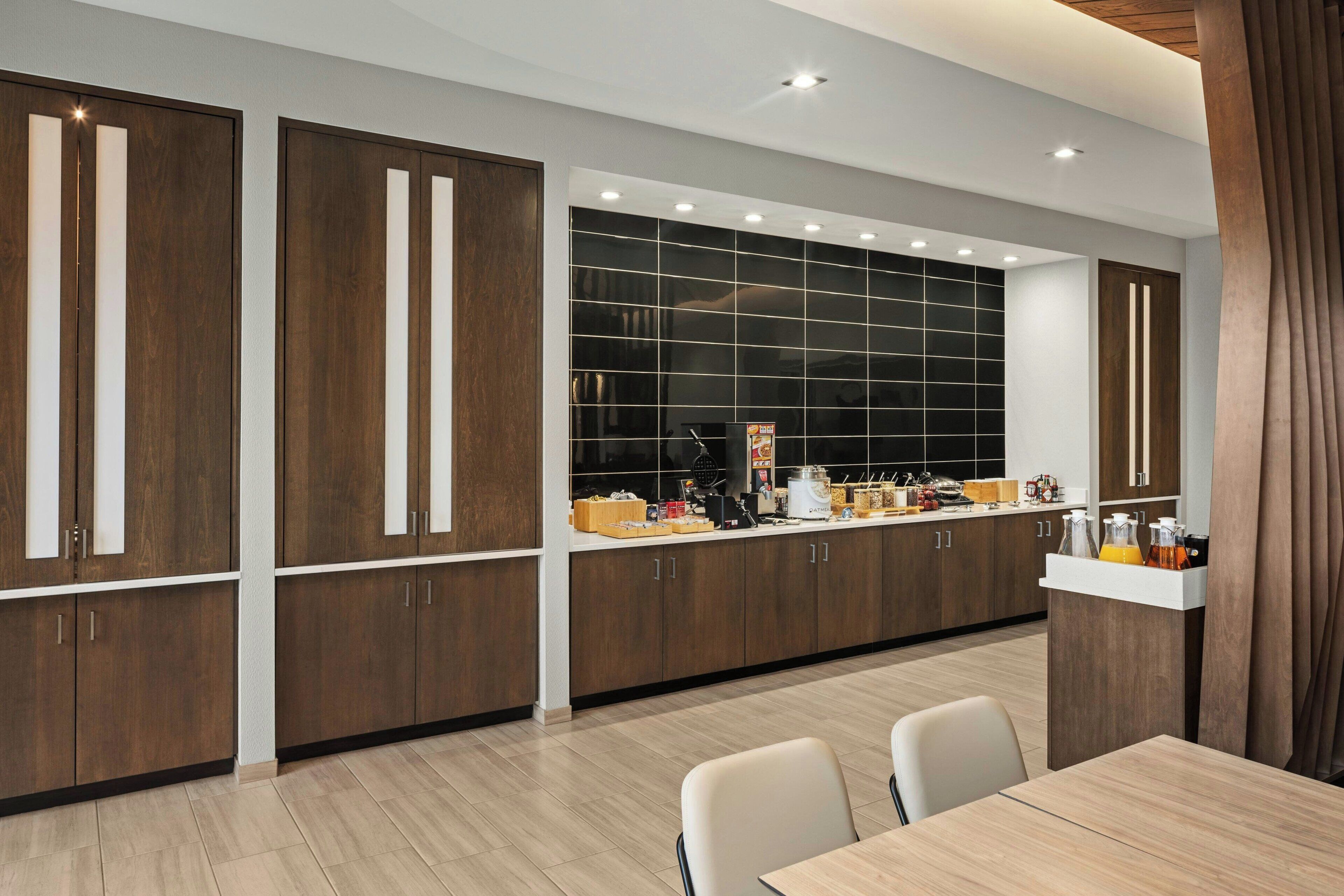 A modern kitchen with wooden cabinets, a large window, and a dining area with chairs.