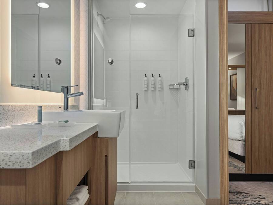 A modern bathroom with a glass-enclosed shower, a vanity with a granite countertop, and a wooden cabinet.