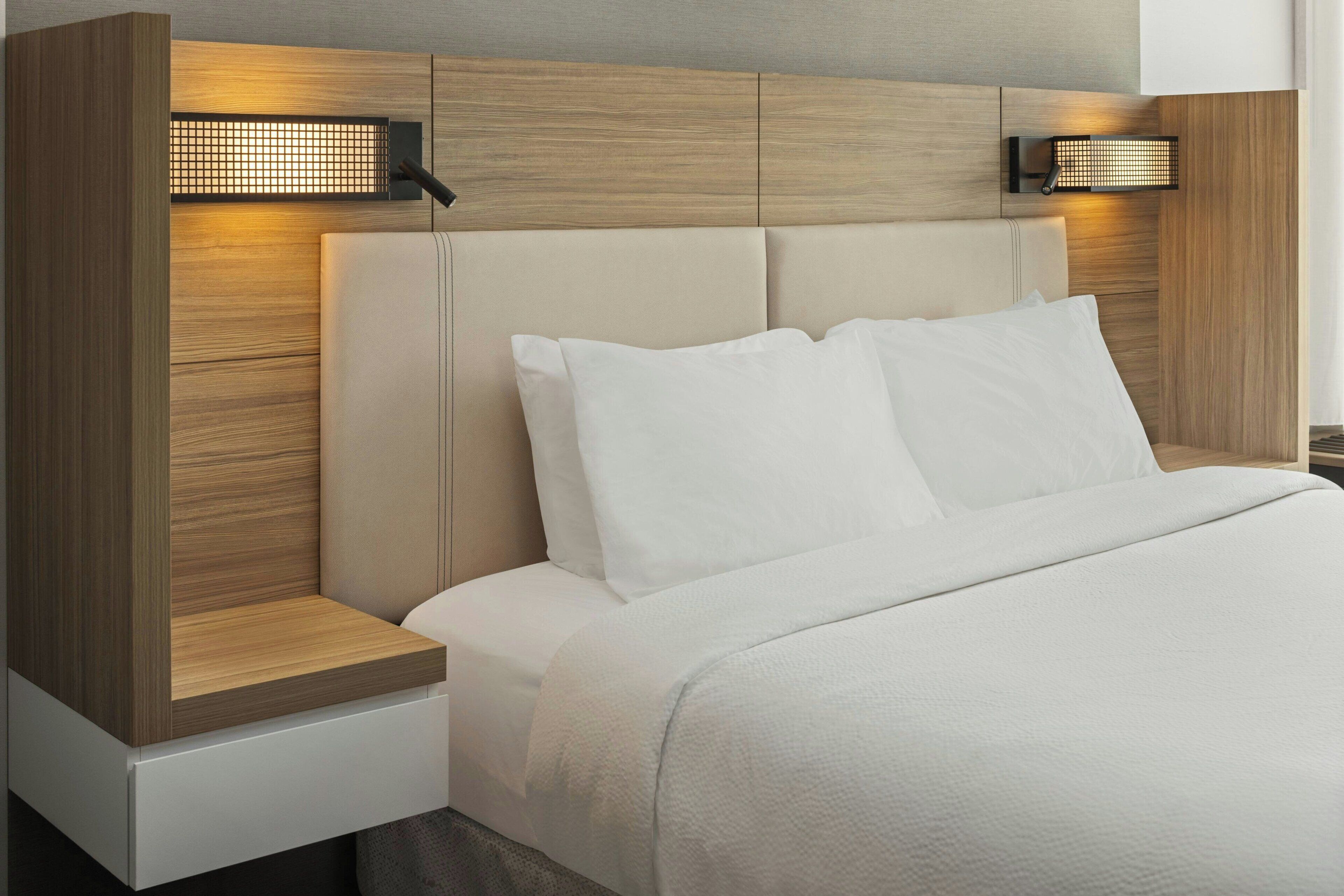 Een moderne slaapkamer met een houten hoofdbord, twee bedlampjes en een net opgemaakt bed.