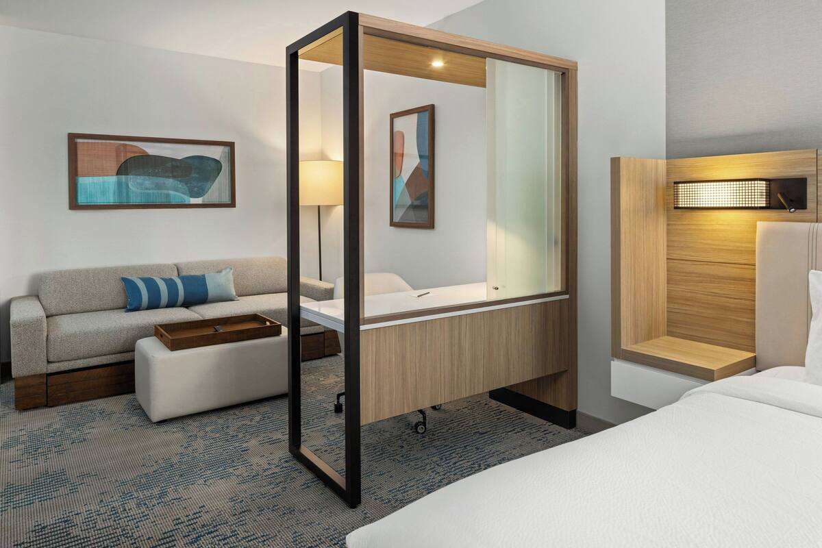 A modern hotel room with a bed, a sofa, a desk, and a large mirror.