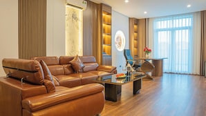 A modern living room with a leather sofa, a glass coffee table, and a dining area with a chair and a vase of flowers. - Núi Vàng Tràng An (Hoa Lu)