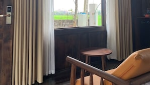 A room with a wooden ceiling, a window with curtains, a wooden chair, and a small round table. - Núi Vàng Tràng An (Hoa Lu)