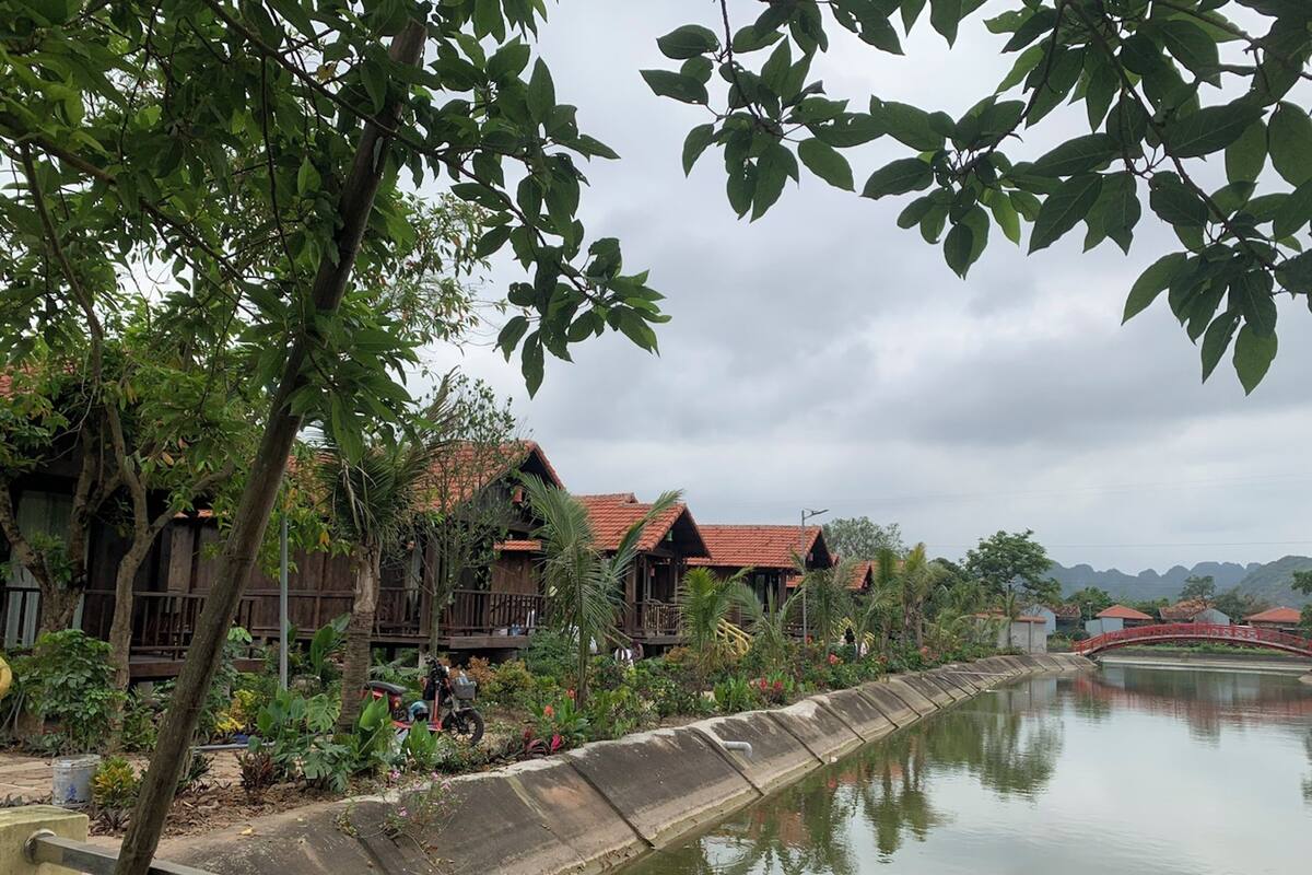 A riverside view with wooden buildings, a concrete embankment, and a bridge.