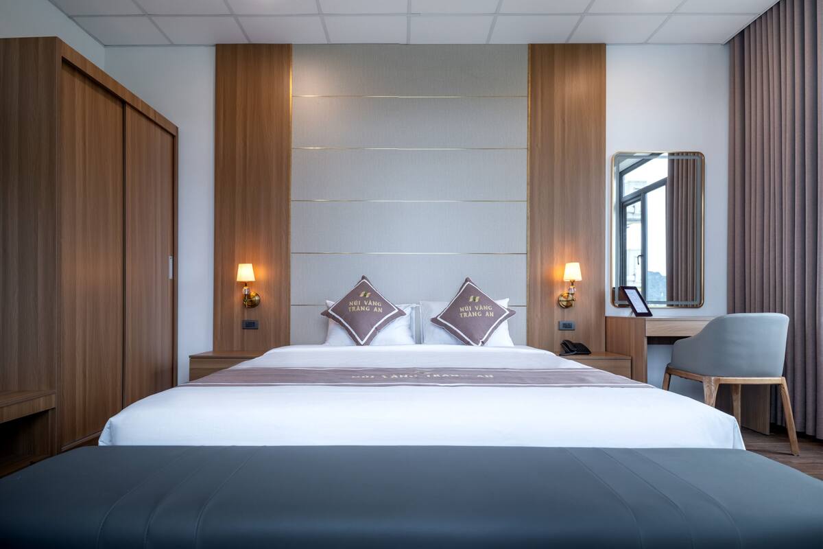 A hotel room with a large bed, two bedside lamps, a desk with a chair, and a large mirror.