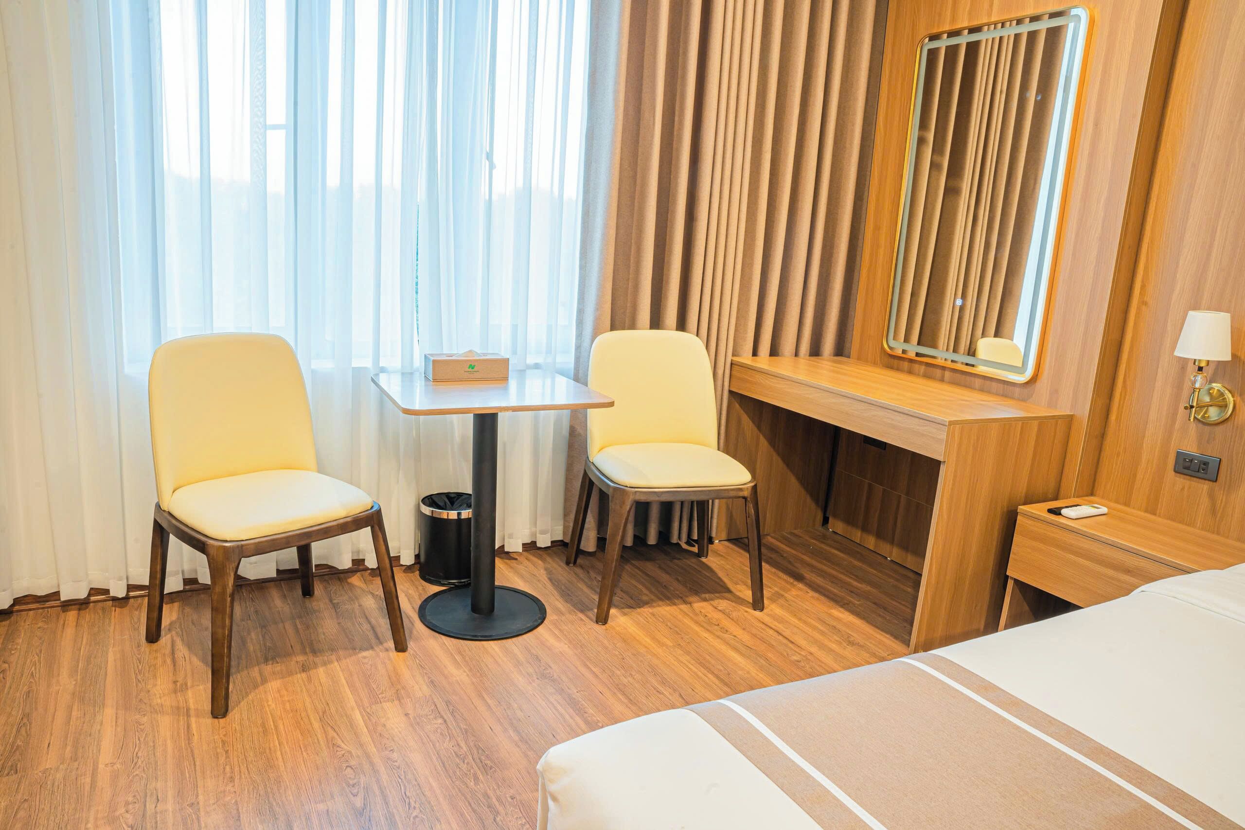 A hotel room with a bed, a desk, two chairs, a small table, a mirror, and a nightstand.