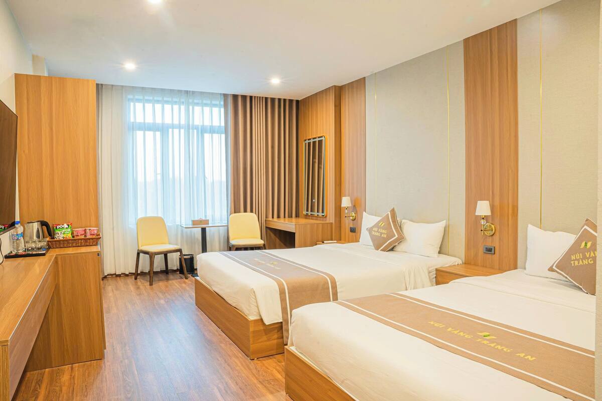 A hotel room with two beds, a desk, a chair, and a TV.