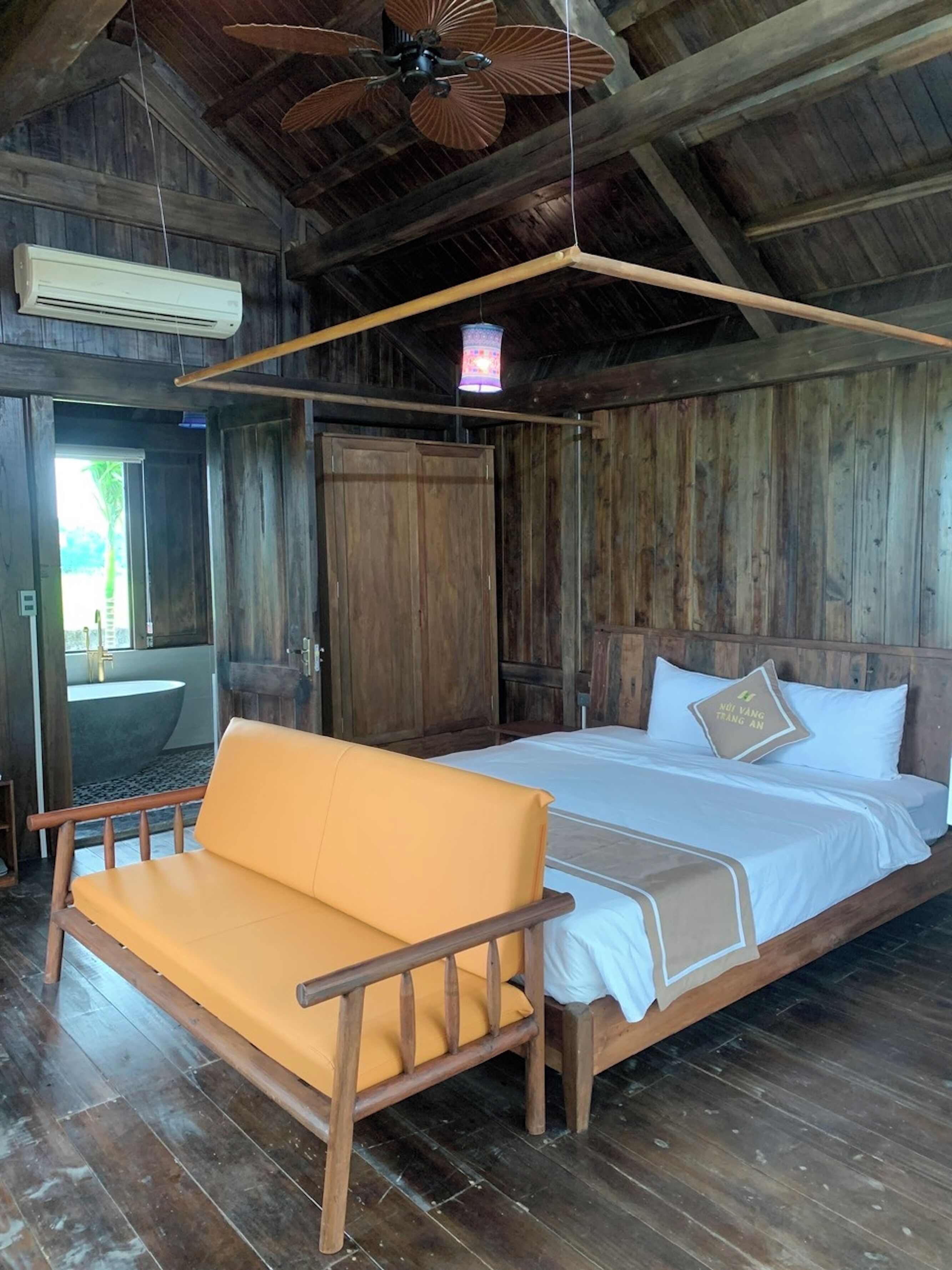Une pièce en bois avec un lit, un banc, un ventilateur de plafond et une fenêtre.