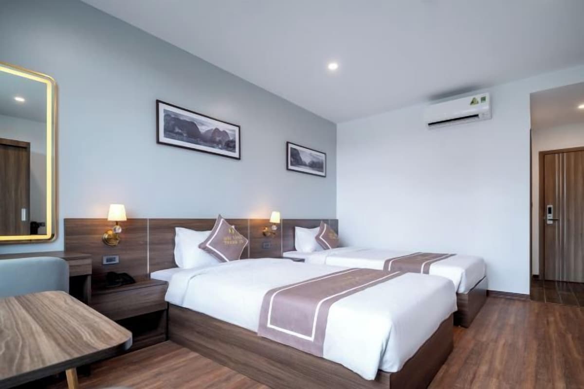 A hotel room with two beds, a desk, a chair, a mirror, and two framed pictures on the wall.