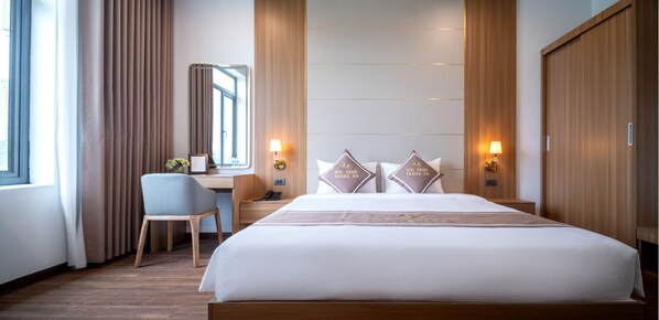 A hotel room with a large bed, a desk, a chair, and two bedside lamps. - Núi Vàng Tràng An (Hoa Lu)