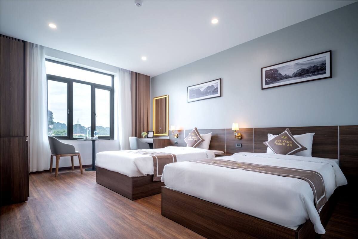 A hotel room with two beds, a desk, a chair, and a large window.