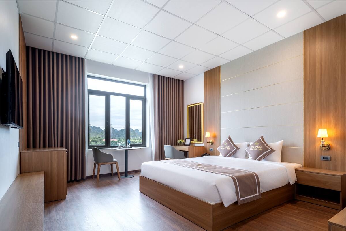 A modern hotel room with a large bed, a desk, a chair, and a TV mounted on the wall.