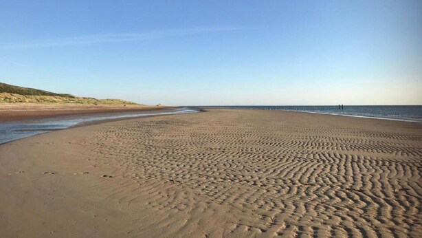 Ein weiter Sandstrand mit sanften Wellen und blauem Himmel.
