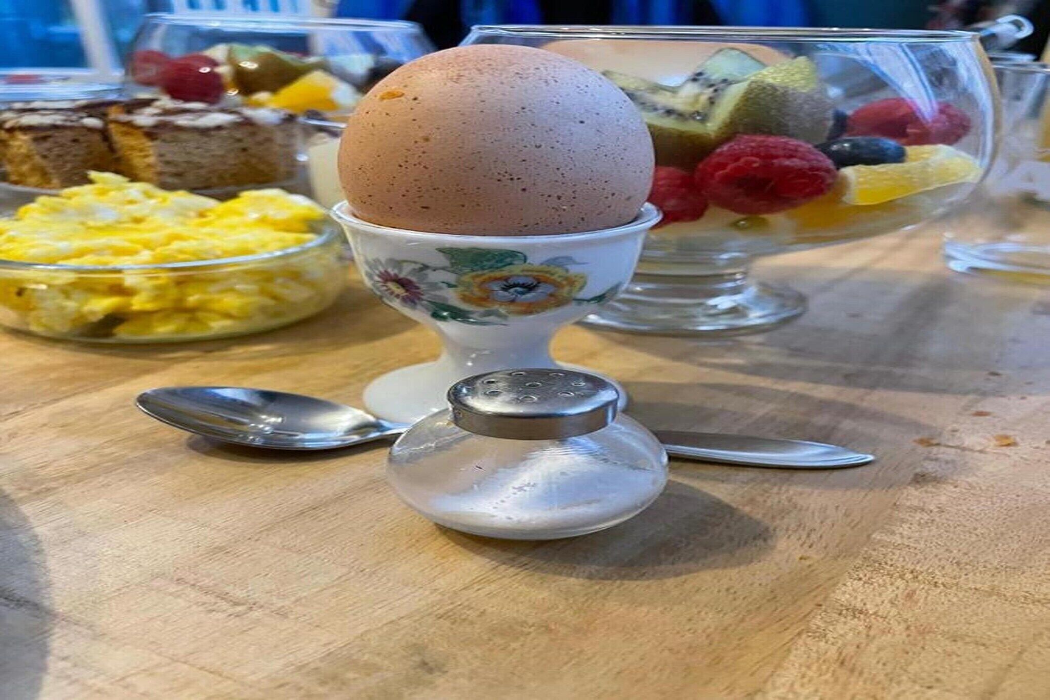 Een dessertbuffet met een groot ei op een bloemenbeker, een kom roerei en een fruitparfait.