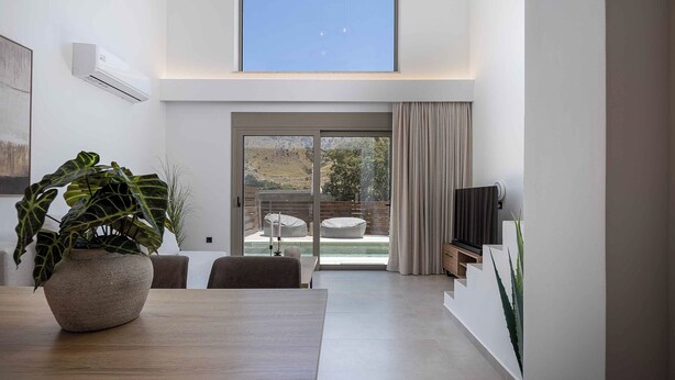 Un salon moderne comprenant une table à manger, une plante en pot, un téléviseur et une porte-fenêtre coulissante donnant sur un espace extérieur.
