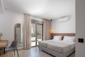 A hotel room with a bed, a chair, a table, a mirror, and a sliding glass door to the outside.
