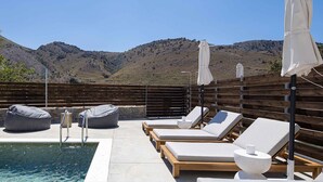 Un espace aménagé au bord de la piscine, avec des chaises longues, des fauteuils en forme de poire et des parasols, offrant une vue sur un paysage montagneux.
