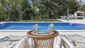 Una piscina con una mesa de mimbre al frente, rodeada de follaje.