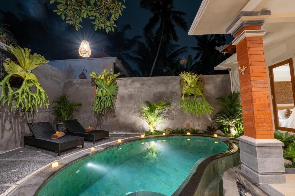 Une piscine entourée d’un mur de briques et de palmiers, avec des chaises longues et des plantes.