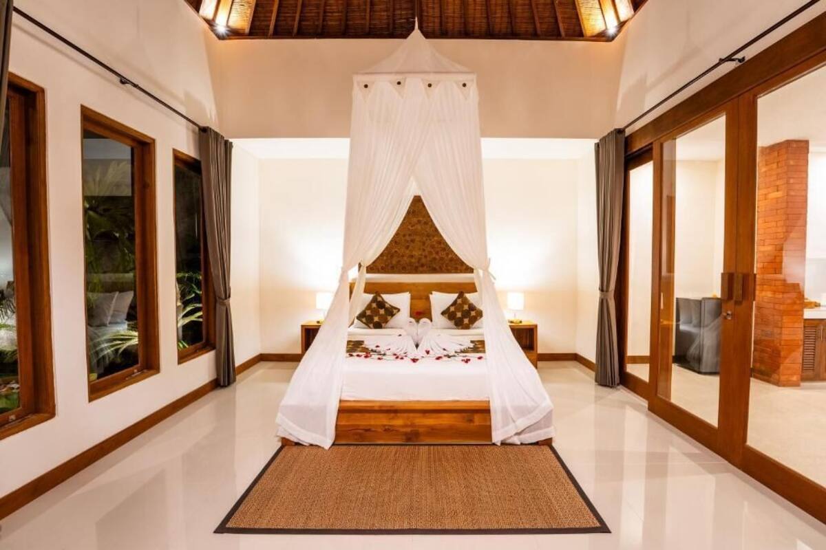Un dormitorio amplio con cama con dosel, ventanas grandes y vistas a una edificación de ladrillo.