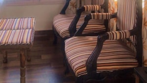 Une pièce avec deux chaises en bois et une petite table, une fenêtre avec des rideaux et une vue sur les arbres à l’extérieur.