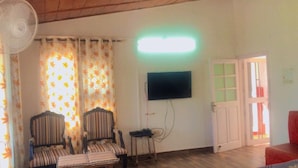Une pièce avec deux fauteuils à rayures, un téléviseur fixé au mur, un ventilateur et une porte donnant sur l’extérieur.