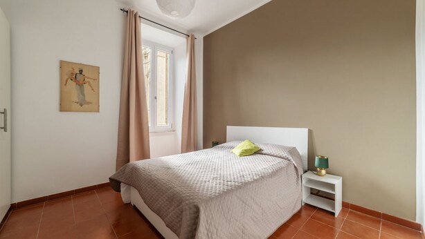 A bedroom with a bed, a nightstand, a lamp, a window with curtains, and a wall-mounted artwork. - GuestHost - Accommodation of 90 sqm on the first floor of a building with elevator, about 10 steps to access (NOT suitable for disabled), ideal for 4 guests.Located in a strategic position two passes from the Vatican and the Sala Nervi, just steps from S (Roma)