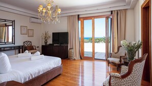 Ein Hotelzimmer mit einem großen Bett, einem Fernseher, einem Schreibtisch, einem Stuhl und Meerblick durch die Schiebetür.