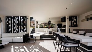 A modern living room with a white sofa, black chairs, a dining table, and a kitchen area with a large island.