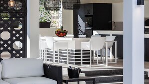 A modern kitchen with white cabinetry, a central island with seating, and hanging black pendant lights.