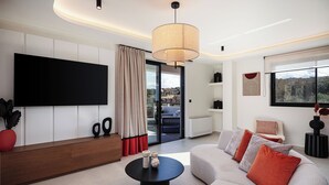 A modern living room with a large flat-screen TV, a sofa with cushions, a coffee table, and a pendant light.