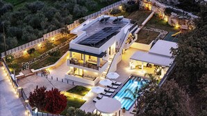 A modern multi-story house with a rooftop solar panel array, a swimming pool, and a landscaped garden.
