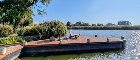Une jetée en bois avec un banc, entourée de verdure et bordée par une étendue d’eau calme.