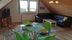 A cozy living room with a glass table, green chairs, a black sofa, and a television on a wooden cabinet. - Charming Attic Retreat, Usedom (Usedom)