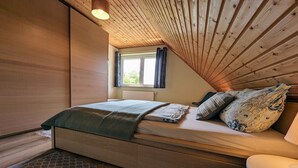 A bedroom with a wooden sloped ceiling, a bed with patterned pillows, a window with curtains, and a radiator. - Charming Attic Retreat, Usedom (Usedom)