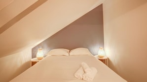 A bedroom with a sloped ceiling, a bed with white linens, two bedside lamps, and a rolled towel on the bed. - Le Villandry beautiful apartment (Tours)