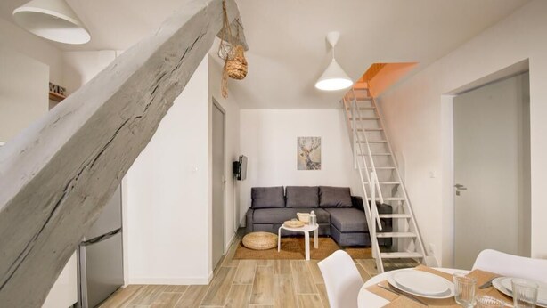 A modern living room with a grey sofa, a dining table set for two, a ladder, and a staircase. - Le Villandry beautiful apartment (Tours)