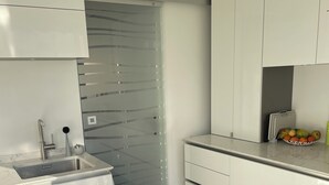 Una cocina moderna con armarios blancos, un lavamanos de acero inoxidable y una puerta de vidrio.