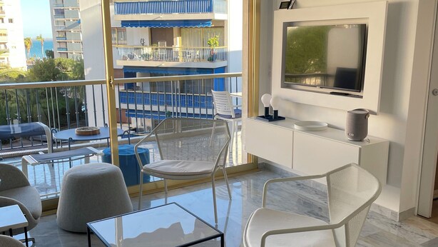 Una sala de estar moderna con balcón, televisión y vista a un edificio con balcones.
