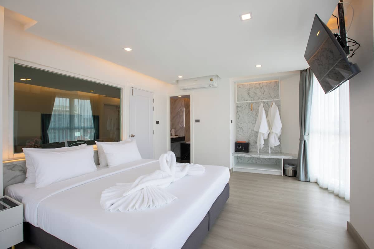 Una habitación de hotel moderna con una cama grande, un televisor montado en la pared y un baño con revestimiento de mármol y un perchero para toallas.