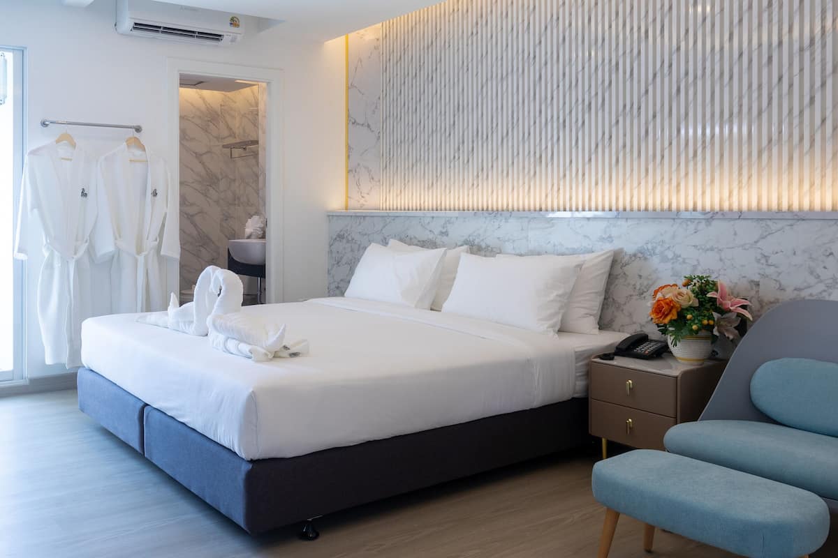 Un dormitorio moderno con una cama grande, una mesita de noche con un teléfono, una silla y una lámpara fijada a la pared.