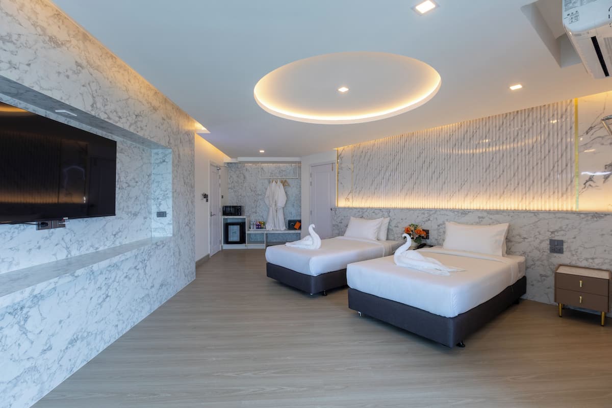 Una habitación de hotel moderna con dos camas, paredes de mármol, un televisor de pantalla plana y una kitchenette pequeña.