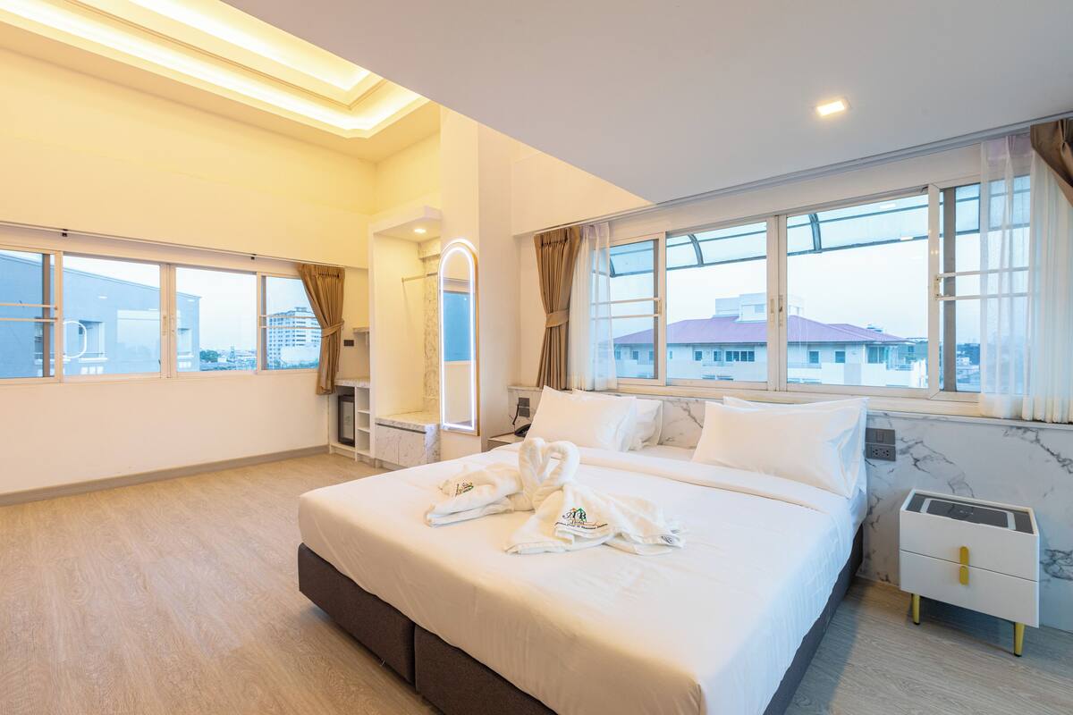 Habitación de hotel moderna con una cama grande, una mesita de noche, un espejo y vistas de la ciudad a través de amplios ventanales.