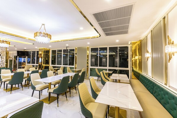 A modern restaurant with green and beige seating, marble flooring, and decorative lighting fixtures.