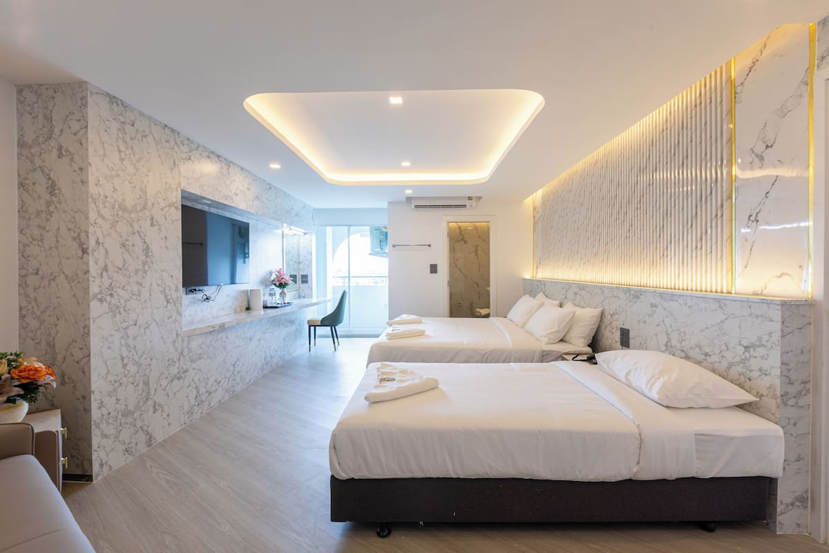Una habitación de hotel moderna con dos camas, paredes de mármol, un espejo grande y un balcón con vistas.